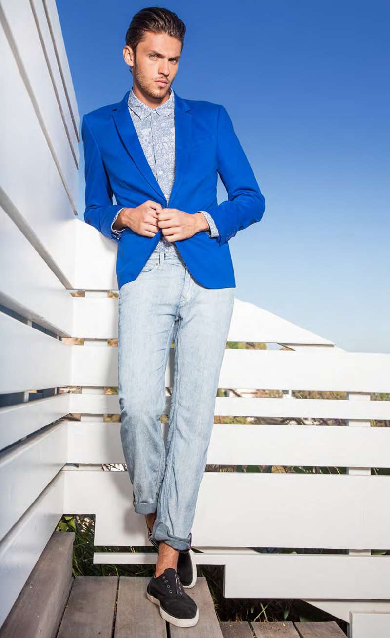 Imagen de un hombre con un look casual y fresco, utilizando una camiseta en tonos azules y blancos, pantalones cortos de mezclilla y zapatos deportivos.